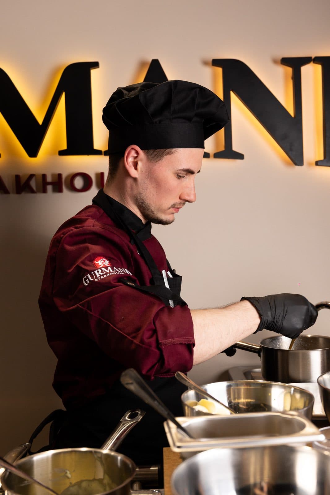Chef gătind în fața peretelui cu logo Gurmand
